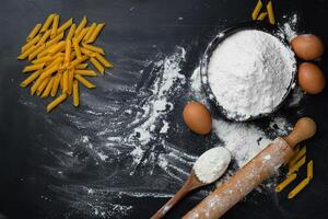 Raw homemade pasta penne on dark background with eggs and flour. Top view. photo