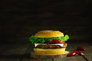 cerca arriba de hamburguesa apilado alto con Fresco coberturas en todo grano artesano bollo, en rústico de madera superficie con oscuro antecedentes foto