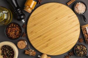 variety of herbs and spices around empty cutting board on gray background, top view. Creative and national cuisine and cooking concept. photo