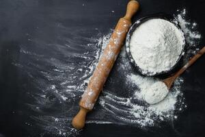 Baking background. Flour and rolling pin on dark table with copy space, top view. World Bread Day photo