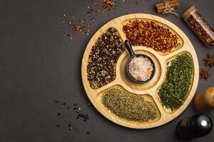 Mix spices on round wooden plate. Coriander seeds, ground red pepper, salt, black pepper, rosemary, turmeric, curry. Top view, close up, gray stone background. photo