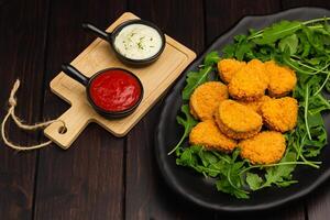 Close-up Nuggets, Dipping Sauce and rocket leaves on a dark background, space for text, selective focus. Fast food. Protein Meals concept. photo