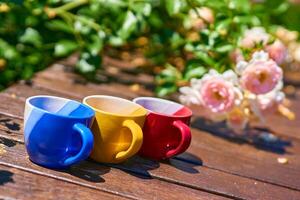 Tea time. Coffee break. Blue red yellow cups on wooden in blooming garden photo