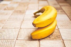 dos maduro amarillo bananas en un anillo en un a cuadros de madera superficie foto