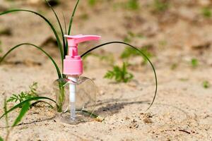 Pink transparent spray bottle for antiseptic and perfume on sand with greenery photo