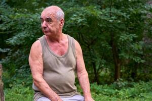 Pensive elderly man pensioner in a T shirt in a forest on a picnic photo