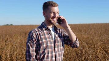 une agriculteur ou agronome pourparlers sur une cellule téléphone dans le milieu de une soja champ pendant récolte video