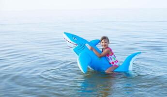 Happy girl of European appearance age of 7 swimming on an inflatable big shark toy in the sea.Family summer vocation concept. Copy space. photo