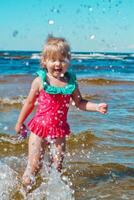 joven contento niño niña de europeo apariencia años de 4 4 teniendo divertido en agua en el playa y salpicaduras, tropicales verano vocaciones,vacaciones.a niño disfruta el mar.vertical foto. foto