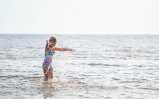 joven contento niño niña de europeo apariencia años de 6 6 teniendo divertido en agua en el playa y salpicaduras, tropicales verano vocaciones,vacaciones.a niño disfruta el familia.mar Días festivos concepto.copiar espacio. foto