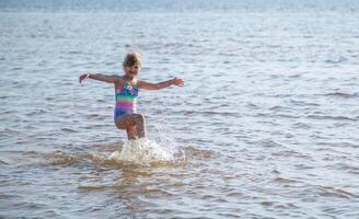 Young happy child girl of European appearance age of 6 having fun in water on the beach and splashing,tropical summer vocations,holidays.A child enjoys the sea.Family holidays concept.Copy space. photo