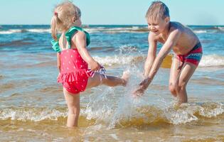 Young happy child girl and boy of European appearance having fun in water on beach and splashing,tropical summer vocations,holidays.A child enjoys the sea.Family summer holidays concept. photo