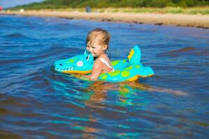Happy girl of European appearance age of 5 swimming on an inflatable crocodile toy in the sea.Kids learn to swim.Little baby girl with inflatable toy float playing in water on summer vocation.Family summer vocation concept. photo