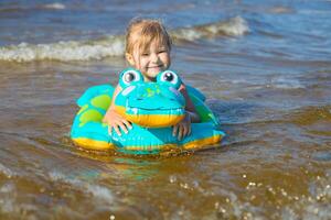 Happy girl of European appearance age of 5 swimming on an inflatable crocodile toy in the sea.Kids learn to swim.Little baby girl with inflatable toy float playing in water on summer vocation.Family summer vocation concept. photo