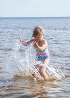 Young happy child girl of European appearance age of 6 having fun in water on the beach and splashing,tropical summer vocations,holidays.A child enjoys the sea.Vertical photo. photo