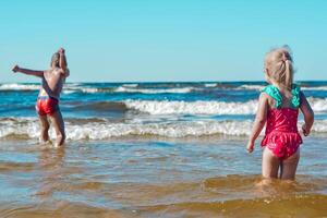 joven contento niño niña y chico de europeo apariencia teniendo divertido en agua en el playa y salpicaduras, tropicales verano vocaciones,vacaciones.a niño disfruta el familia.mar Días festivos concepto.copiar espacio.atrás vista. foto