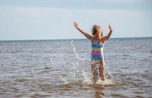 joven contento niño niña de europeo apariencia años de 6 6 teniendo divertido en agua en el playa y salpicaduras, tropicales verano vocaciones,vacaciones.a niño disfruta el familia.mar Días festivos concepto.copiar espacio. foto