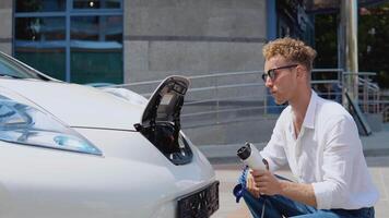 A young curly man disconnects the electric car from the charger video