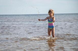 joven contento niño niña de europeo apariencia años de 6 6 teniendo divertido en agua en el playa y salpicaduras, tropicales verano vocaciones,vacaciones.a niño disfruta el familia.mar Días festivos concepto.copiar espacio. foto