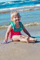 Young happy child girl of European appearance age of 4 having fun on the beach ,laughing and looking at the camera,tropical summer vocations,holidays.A child enjoys the sea.Vertical photo