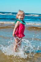 joven contento niño niña de europeo apariencia años de 4 4 teniendo divertido en agua en el playa y salpicaduras, tropicales verano vocaciones,vacaciones.a niño disfruta el mar.vertical foto. foto
