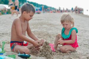 Brother and sister making sand castle on the beach in warm summer day.Family summer holidays concept. High quality photo