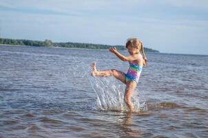 Young happy child girl of European appearance age of 6 having fun in water on the beach and splashing,tropical summer vocations,holidays.A child enjoys the sea.Family holidays concept.Copy space. photo