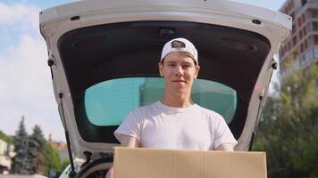 Moving and delivery of manufactured goods. An employee holds a box in his hands and stands next to a car filled with parcels. Express delivery video