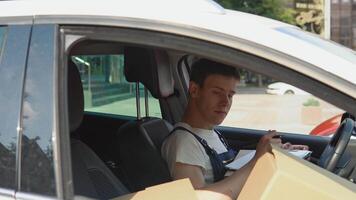 Moving and delivery of manufactured goods. The driver fills in the cargo documents. Many craft boxes are stacked in the passenger seat next to the driver. Delivery of goods home video