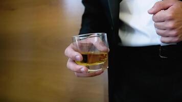 Attractive business man with a glass of whiskey in a brown room. Businessman holding whiskey video