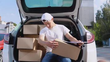 The courier sits on the edge of the open trunk, filled with boxes of goods and fills out documents. Delivery of goods home video