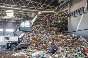 Excavator on primary sorting of garbage at waste processing plant. Separate garbage collection. Recycling and storage of waste for further disposal. photo