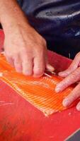 Hand cutting salmon on red board in closeup gesture video