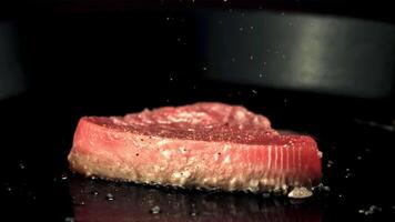 super lento movimento tonno bistecca è fritte nel un' frittura padella. su un' nero sfondo.filmato su un' alta velocità telecamera a 1000 fps. video