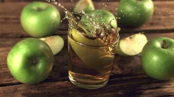 súper lento movimiento un pedazo de verde manzana con salpicaduras caídas dentro un vaso de jugo. en un de madera antecedentes. filmado en un alta velocidad cámara a 1000 fps. video