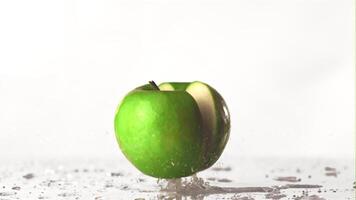 el súper lento movimiento verde manzana caídas en el mesa y divisiones dentro medio. en un blanco antecedentes. filmado en un alta velocidad cámara a 1000 fps. alto calidad full HD imágenes video