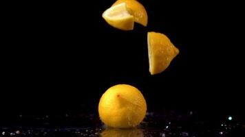 Super slow motion pieces of fresh lemon fall on the table with splashes of water. On a black background.Filmed on a high-speed camera at 1000 fps. High quality FullHD footage video