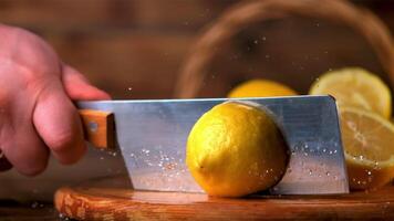 Super slow motion the male hand with a knife cuts the lemon into two halves. On a wooden background. Filmed on a high-speed camera at 1000 fps. High quality FullHD footage video