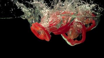 Super slow motion pieces of red sweet pepper fall into the water with splashes.Filmed at 1000 fps. On a black background. High quality FullHD footage video