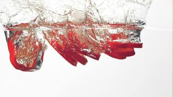 Super slow motion pieces of red sweet pepper fall into the water with splashes. Filmed at 1000 fps.On a white background. video