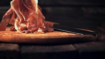 súper lento movimiento rebanado dentro Delgado piezas de jamón caídas en un corte tablero con un cuchillo.filmado a 1000 fps. en un de madera antecedentes. video