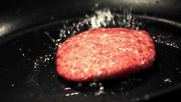 The super slow motion raw burger falls on the pan with a splash of oil. Filmed at 1000 fps.On a black background. video