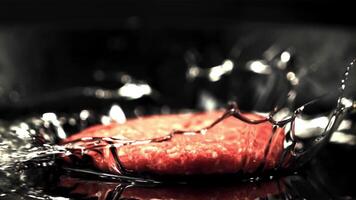 The super slow motion raw burger falls on the pan with a splash of oil. Filmed at 1000 fps.On a black background. video