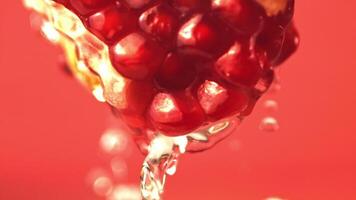 Super slow motion with a piece of pomegranate drains water. On a red background. Filmed on a high-speed camera at 1000 fps. High quality FullHD footage video