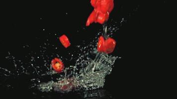 Super slow motion chopped chilli pepper falls on the water with splashes. On a black background. Filmed on a high-speed camera at 1000 fps. High quality FullHD footage video