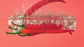 Super slow motion red chili pepper falls into the water with splashes. On a pink background.Filmed on a high-speed camera at 1000 fps. High quality FullHD footage video