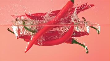 Super slow motion chilli pepper falls into the water with splashes. On a pink background. Filmed on a high-speed camera at 1000 fps. High quality FullHD footage video