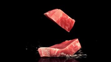 Super schleppend Bewegung zwei roh Thunfisch Steaks fallen auf das Tabelle mit spritzt von Wasser. auf ein schwarz Hintergrund.gefilmt auf ein schnelle Geschwindigkeit Kamera beim 1000 fps. video