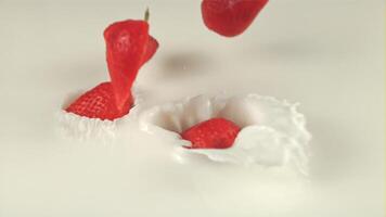 Super slow motion halves of strawberries fall with splashes in milk. Macro background. Filmed on a high-speed camera at 1000 fps video