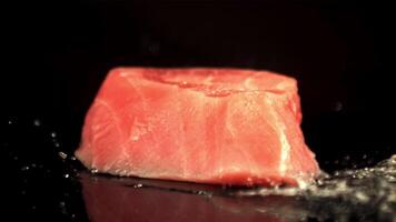 Super slow motion raw piece of tuna falls on the table with splashes of water. On a black background. Filmed on a high-speed camera at 1000 fps. video